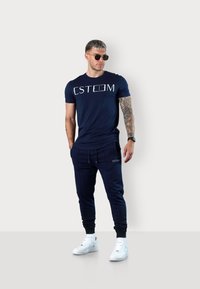 Navy blue t-shirt with "ESTEEM" printed in white, paired with navy joggers featuring side pockets and a fitted cuff. White sneakers.