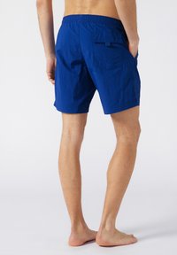 Shorts de bain bleus en tissu léger, avec une taille élastique et une poche arrière à rabat. Texture lisse, design jusqu'aux genoux.
