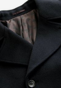 Abrigo de mezcla de lana negro con gran cuello, que presenta un forro de satén suave con un patrón geométrico y un cierre de botón único.