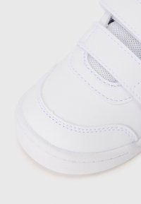 Baskets blanches avec une tige en cuir lisse, des sections en mesh, des bandes Velcro et un bout rond avec de subtils détails de couture.