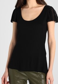 Czarny top z krótkim rękawem, z okrągłym dekoltem i przezroczystym, fakturowanym materiałem na rękawach. Gładka, luźna fason.