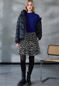 Sort puffjakke, blå sweater og grå dyreprint nederdel med flæser. Sorte tætsiddende strømpebukser og kraftige sorte støvler fuldender outfittet.