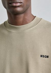 Felpa khaki con scollatura rotonda, texture a coste e piccolo logo MSGM nero sul lato sinistro. Finitura del tessuto morbida.