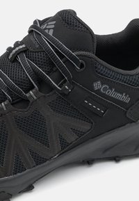Gros plan sur une chaussure de randonnée Columbia noire avec tissu mesh, empiècements à motifs, lacets et logo Columbia sur le côté et la languette.