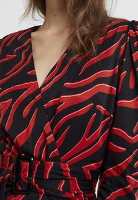 Rotes und schwarzes Wickelkleid mit einem Wellenmuster, glatter Textur und tailliertem Schnitt, versehen mit einem dicken schwarzen Gürtel.