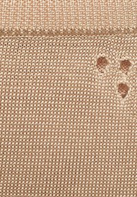 Knit fabric in a soft beige color featuring a loose texture and small decorative holes creating a pattern. Even stitching visible.