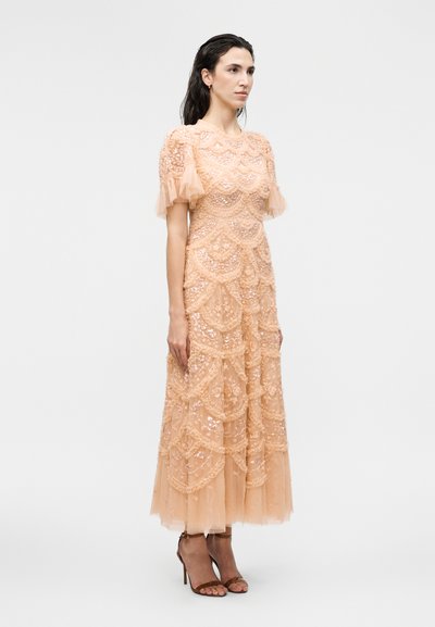 Γυναίκα που φοράει ένα ροζέμπορτ μίντι φόρεμα με παγιέτες, φουσκωτά μανίκια και στρωμένη τούλινη κορυφή, με καφέ πέδιλα με τακούνι.