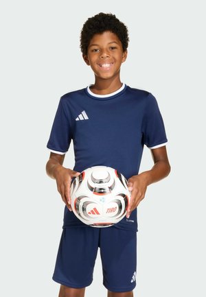 Navy sports shirt and shorts with white accents, holding a patterned soccer ball. The shirt features three white stripes on the left chest.