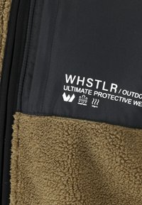 Brun fleece-stof med en struktureret overflade, parret med en sort glat stofsektion, der har hvid trykt branding og symboler.