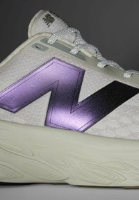 Urheilukenkä, jossa on karhea vaaleanharmaa päällinen, jossa on näkyvä violetti geometrinen muotoilu ja mustat yksityiskohdat. Paksu kermaisa pohja, jossa on aaltoilu.