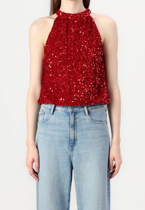 Czerwony top na szyję z cekinami i teksturowanym wykończeniem, zestawiony z jasnobłękitnymi, wysokim stanem jeansami. Prosty dekolt, krótki krój.