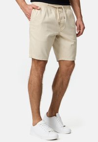 Beige bomuldsshorts med elastisk talje, justerbar snor og sidelommer; glat tekstur og knælangt design.