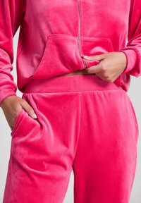 Roze velours trainingspak met een rits hoodie met kangoeroezak en bijpassende broek met zijzakken, zachte textuur, relaxte pasvorm.