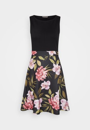 Zwarte mouwloze jurk met een aansluitende top en een uitlopende bloemenrok met roze en witte bloemen op een donkere achtergrond.