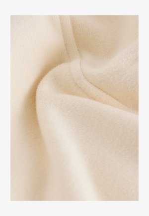 Krämfärgat tyg med en mjuk, texturerad yta, med subtila variationer och veck som antyder ett lätt, stickat material.