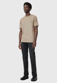 Beige short-sleeve shirt with a round neckline, paired with dark gray jeans and black boots, featuring a subtle logo on the shirt.