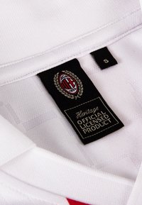 Witte sportshirt met een kraag, met zwart en rood AC Milan-logo op een geweven zwart label, gemarkeerd met "S" voor maat. Geweven stofdetails zichtbaar.