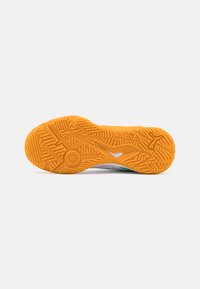 Skoens såle med en teksturert oransje gummi såle som har sikksakkmønstre og en sentral sirkulær aksent, plassert mot en hvit bakgrunn.