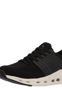Zapatilla deportiva negra con parte superior de tejido de punto, cordones negros, panel lateral de soporte y suela ventilada blanca.