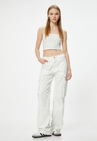 Pantaloni cargo bianchi realizzati in tessuto leggero, con molteplici tasche, una vestibilità rilassata e dettagli di cucitura sottili. Abbinati a un top bianco cropped.
