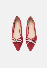 Czerwone baleriny zamszowe z ostrym noskiem i płaską podeszwą, ozdobione srebrną kokardą z przodu oraz beżową wkładką.