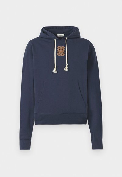 Zila kapuce no kokvilnas ar priekšējo kabatu, kapuces saites ar bumbām un brūnu izšūtu logo uz krūtīm.