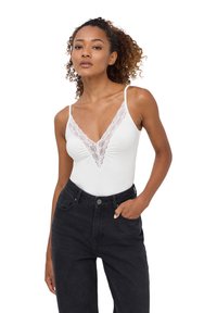 Body bianco con scollatura a V in pizzo e spalline sottili, abbinato a jeans neri a vita alta. Tessuto morbido con una silhouette aderente.