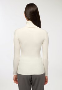 Dopasowany biały sweter z prążkowanego materiału z długimi rękawami, gładka faktura i zaokrąglony dół, w połączeniu z szarymi spodniami.