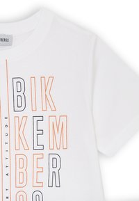T-shirt in cotone bianco con stampe verticali in arancione e testo nero. Maniche corte e scollatura rotonda. Design semplice e moderno.