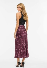 Top negro sin mangas combinado con una falda larga burdeos con grandes lunares rosas, textura suave y silueta fluida.