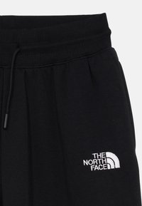 Črne trenirke z rebrastim pasom, zapiranjem na vrvico in belim izvezenim logotipom The North Face na levem stegnu.