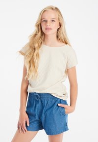 Světle béžový texturovaný top s krátkým rukávem v kombinaci s modrými šortkami ve stylu denim, které mají elastický pas a boční kapsy.