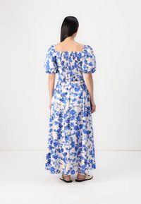 Robe maxi en tissu léger avec des motifs floraux bleus sur fond blanc. Dotée de manches bouffantes et d'un dos smocké.