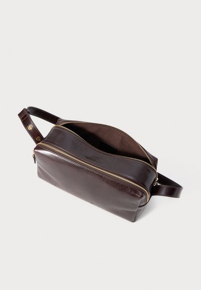 Σκούρο καφέ δερμάτινη τσάντα με φερμουάρ, ορθογώνιο σχήμα και έναν πλευρικό ιμάντα. Ο εσωτερικός χώρος είναι επενδεδυμένος με σουέντ. Χρυσές μεταλλικές λεπτομέρειες.