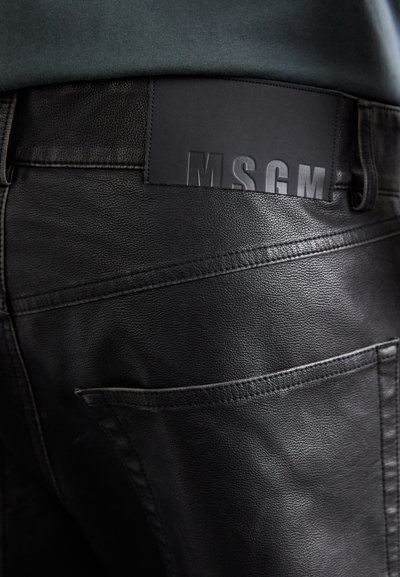 Pantalones de cuero negros con un acabado mate, costuras visibles y un parche de logo texturizado negro etiquetado "MSGM" en la cinturilla.