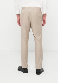 Beige nadrág, könnyű anyagból, szabott fazonnal. Két hátsó zsebével rendelkezik, gombos záródással, és sima textúrájú.