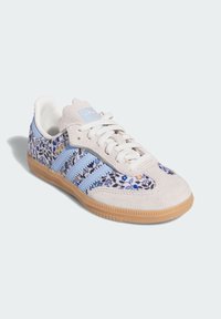 Hellgraue Wildleder-Sneaker mit einem floralen Muster in Blau und Weiß, ausgestattet mit drei hellblauen Streifen und einer Gummi-Außensohle.