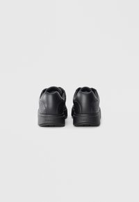 Black sneakers with a textured back, rounded shape, and a smooth matte finish. Features a branded heel and a cushioned sole for comfort.