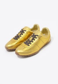 Złote sneakersy wykonane z metalicznego materiału, z ciemnobrązowymi sznurowadłami, zaokrąglonym noskiem, teksturowaną gumową podeszwą i prostym, przeszywanym wzorem.