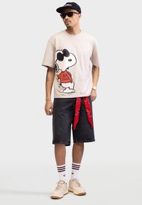 Beige t-särk, millel on Snoopy graafika prillidega, mustad denimsü shorts, punane sall, valged sokid tumepunaste triipudega ja beežid jooksujalatsid.