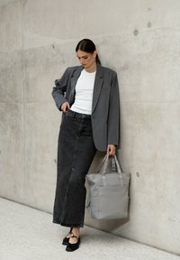 Grå skräddarsydd kavaj över en vit T-shirt, tillsammans med en lång svart denimkjol. Bär en ljusgrå axelväska. Platta svarta skor.