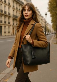 Sac en toile noir en cuir avec une finition texturée et un accent de gland, porté par une personne vêtue d'un manteau et d'un pull marron dans une rue.