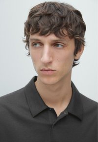 Donkergrijs poloshirt met een kraag en drie knopen. Slank model, zachte textuur, model heeft halflang golvend haar.