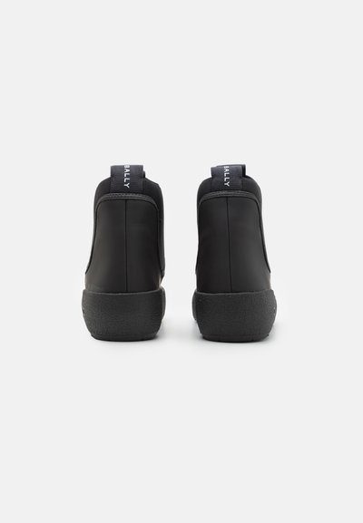 Adidași negri din piele cu glezna înaltă, cu o talpă din cauciuc texturat, având un design cusut și mânere la spate pentru a facilita îmbrăcarea.