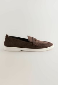Mocassin en daim brun avec une bride à boucle et une semelle en caoutchouc blanche, présenté de profil sur un fond uni.