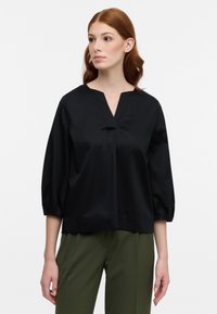 Blusa nera con scollatura a V e maniche a tre quarti a palloncino. Tessuto morbido, vestibilità comoda e dettaglio di cucitura sottile lungo la parte anteriore.
