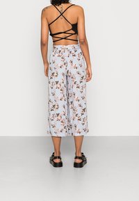 Floral-patterned blue culottes with a flowy texture and an elastic waistband, paired with a black strappy crop top and chunky black sandals.