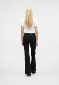 Haut blanc ajusté à manches courtes associé à un jean noir évasé. Le jean présente un design à cinq poches et une texture lisse.