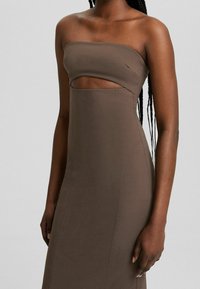 Robe marron ajustée sans bretelles avec une découpe frontale, portée par une personne aux cheveux longs tressés sur un fond uni.