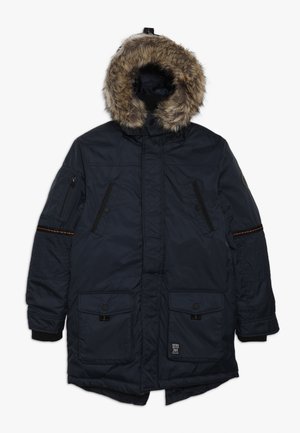 Námořnická modrá zimní parka s kapucí podšitou kožešinou, několika kapsami na zip a knoflíky, žebrovanými manžetami a oranžovými švy na rukávech.